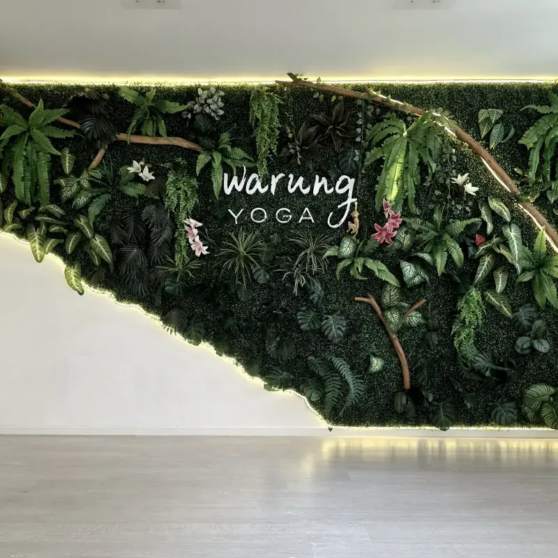 Pflanzenwand mit Warung-Yoga-Logo im Kursraum